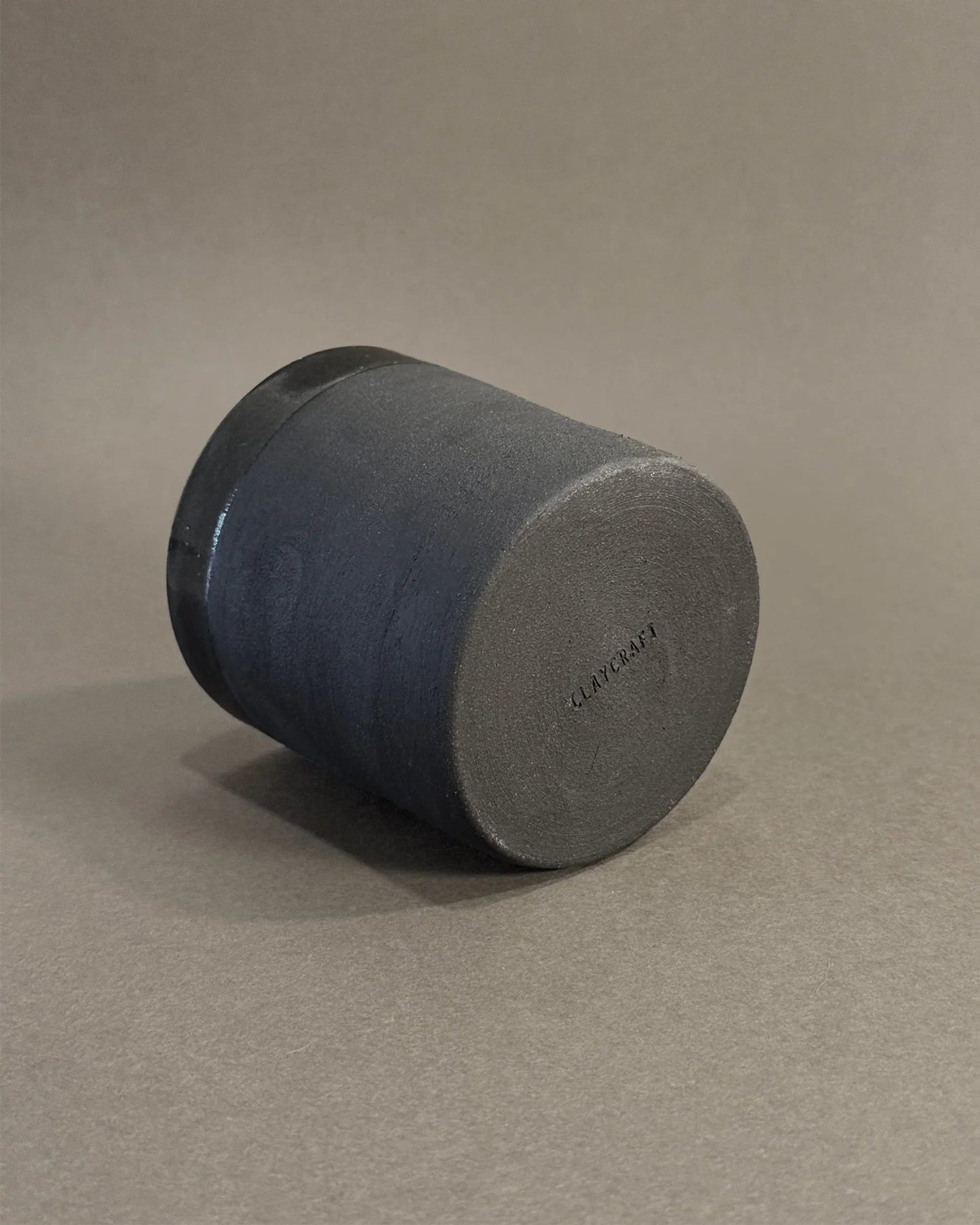 Black ceramic cup upside down on gray surface with embossed CLAYCRAFT logo on the bottom