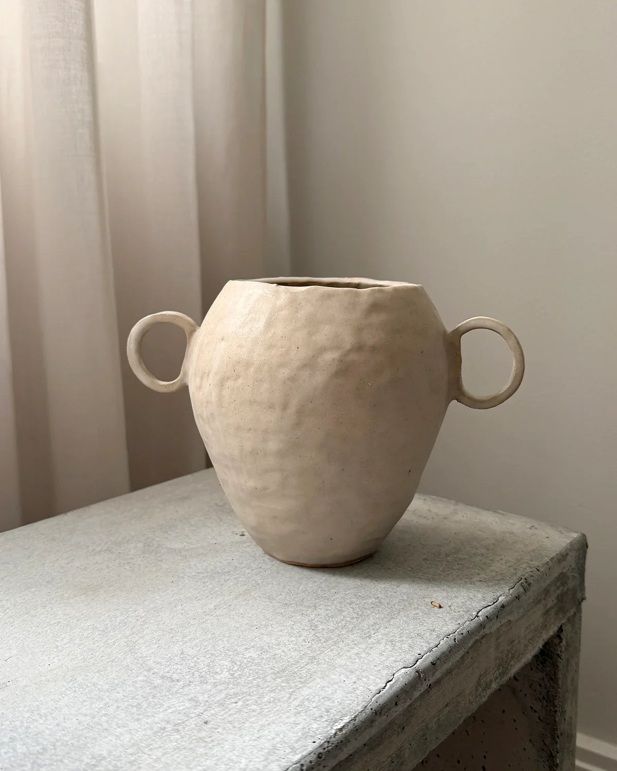 Handmade beige ceramic vase with two loop handles on rustic concrete table in minimal room