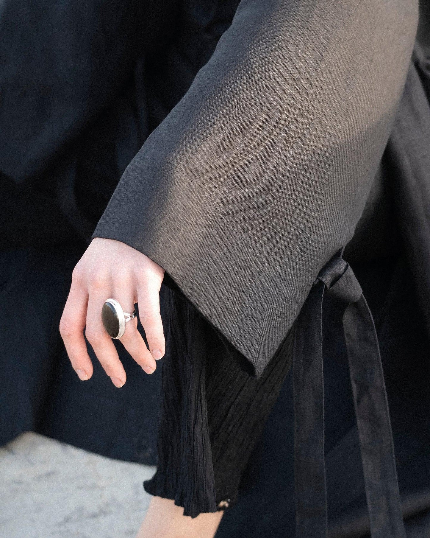 Close-up of a hand wearing a silver black stone ring, draped in a dark textured fabric with a tie detail