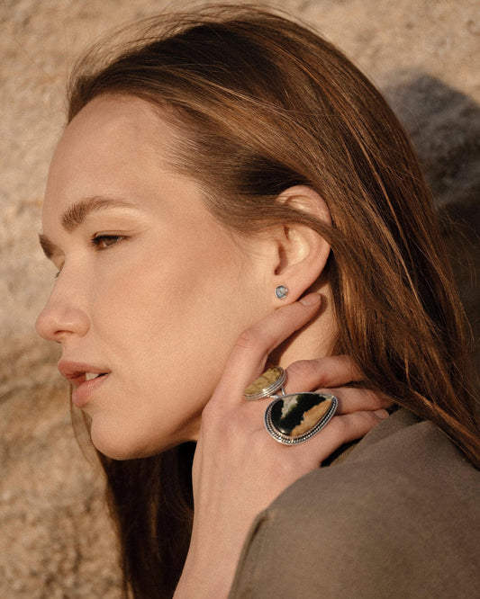 Profile of woman with brown hair wearing silver gemstone earrings and large silver rings in natural sunlight