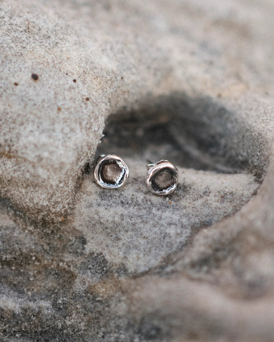 Close-up of rustic silver stud earrings on textured natural stone background