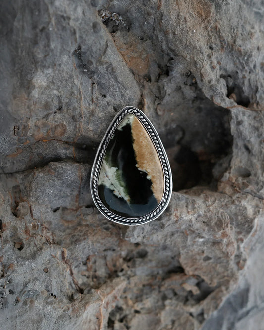 Teardrop-shaped agate stone ring with silver twisted rope setting on rough gray rock