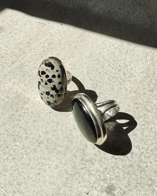 Two sterling silver , gemstone rings on a concrete surface, one with a Dalmatian jasper stone and the other with a smooth black stone