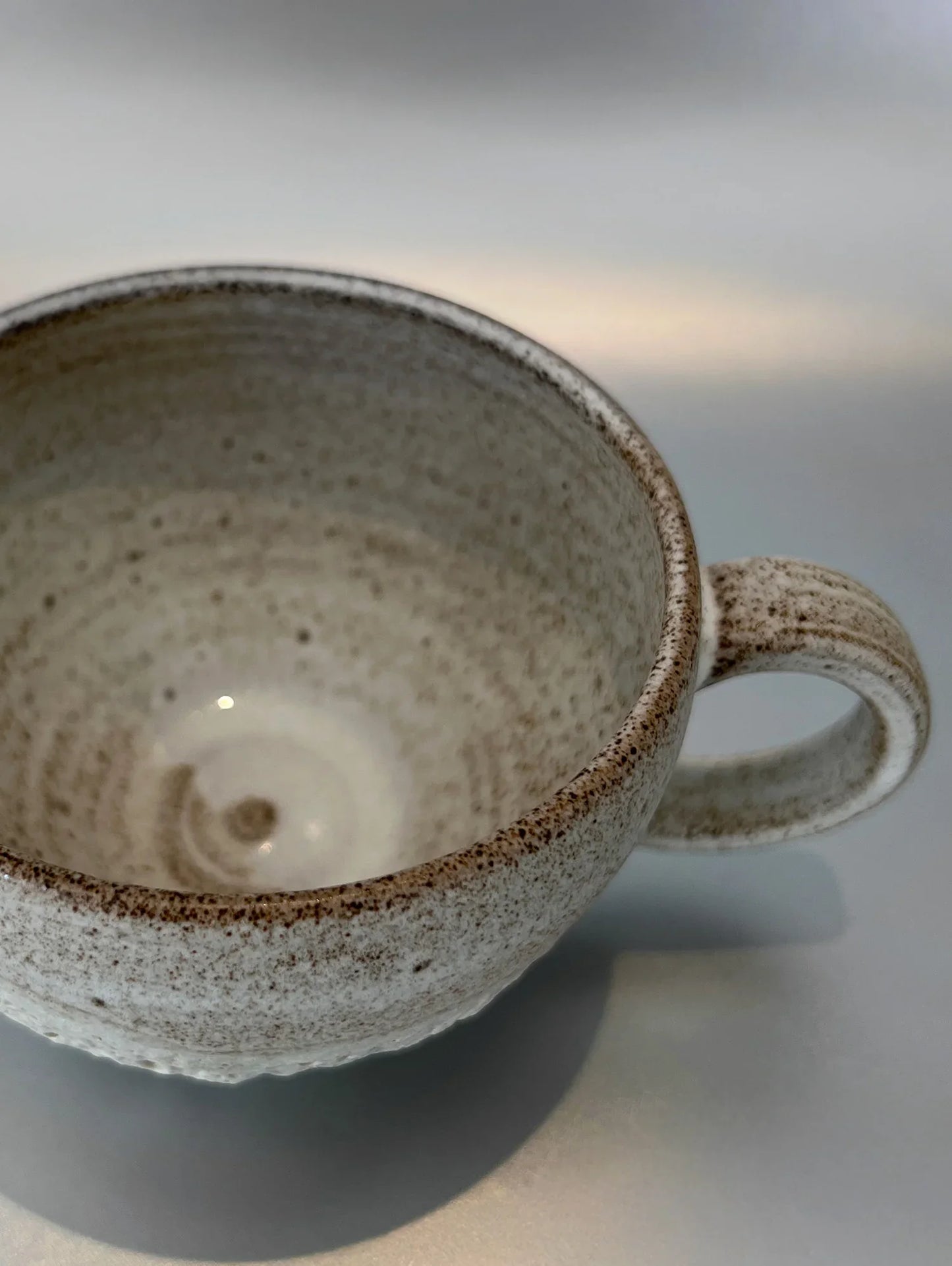 Speckled ceramic cup with handle on a light surface, close-up detail of texture