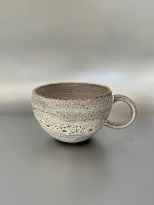 Handmade ceramic coffee cup with textured white and brown glaze on neutral background