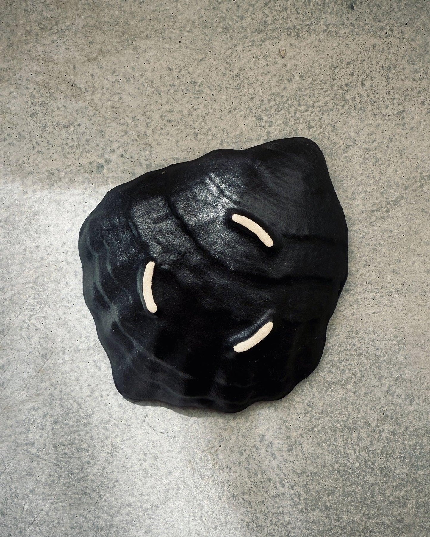 Black ceramic oyster shell plate with three beige indentations on concrete background