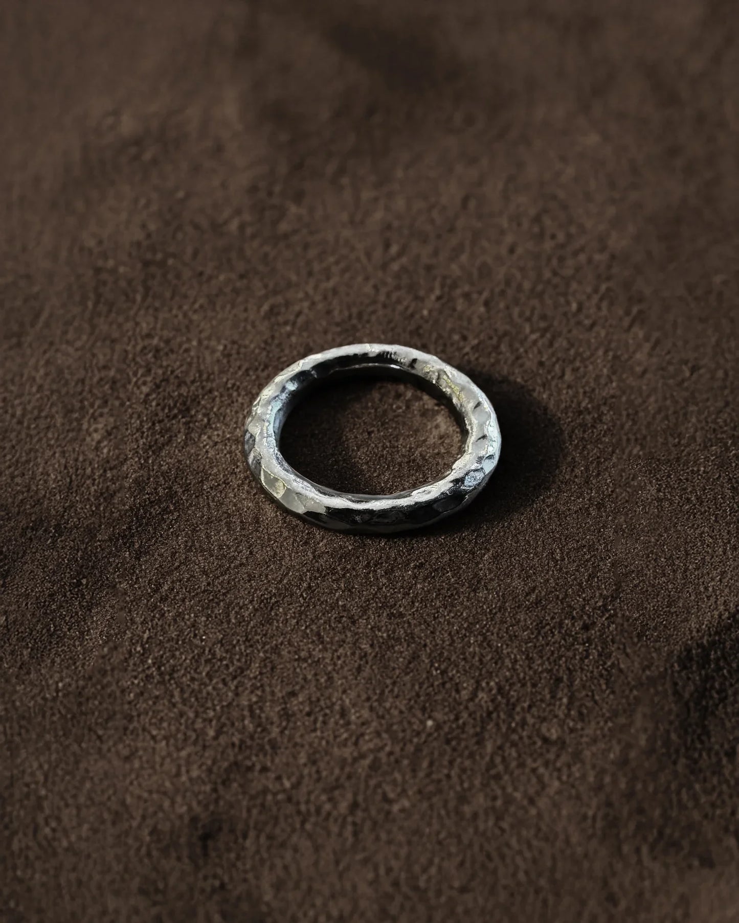 Handcrafted hammered silver band ring on textured brown fabric background