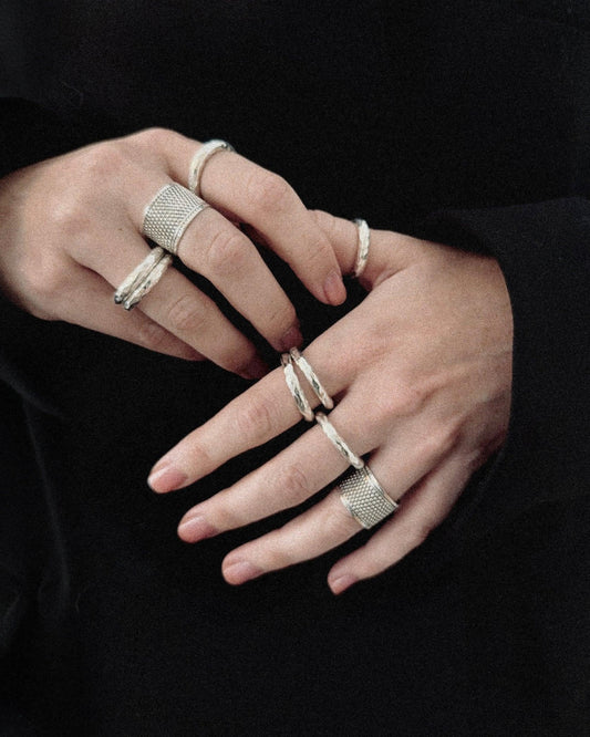 Hands wearing multiple silver rings with textured designs on a black background