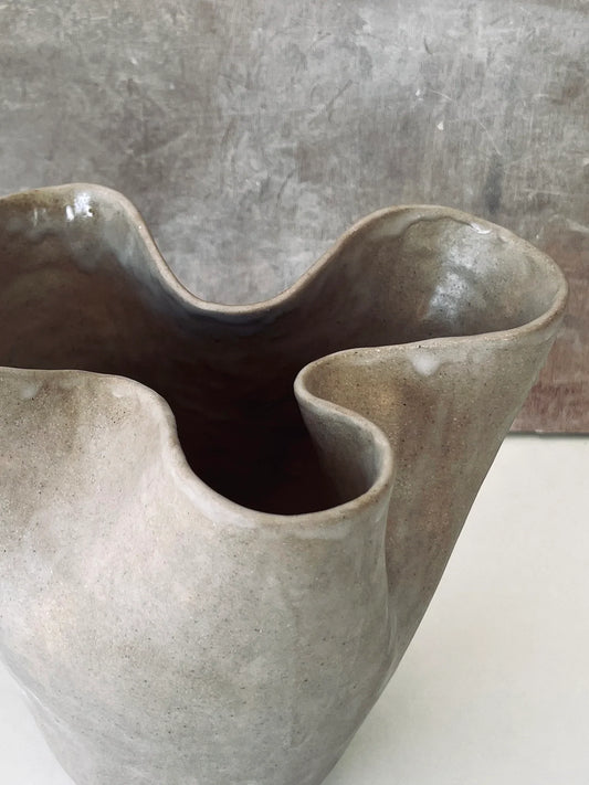 Close-up of a beige wave-shaped ceramic vase with a glossy finish on a light surface