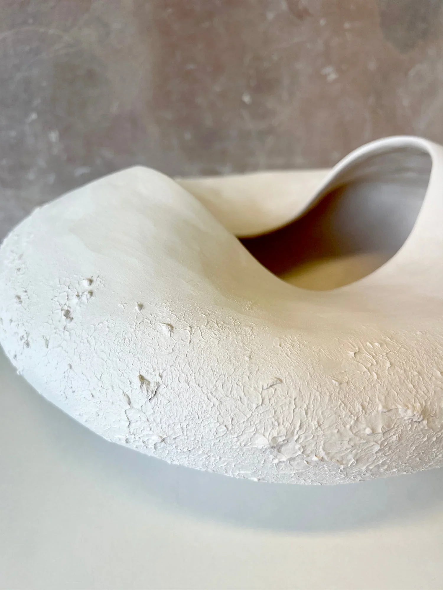 Close-up of a white textured ceramic molten bowl with a smooth curved opening on a neutral background