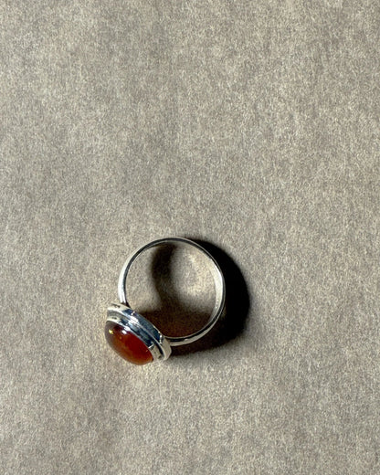 Silver ring with a red amber stone on a grey surface