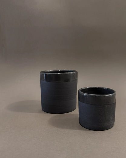 Two black ceramic cups with matte and glossy finishes on a neutral background
