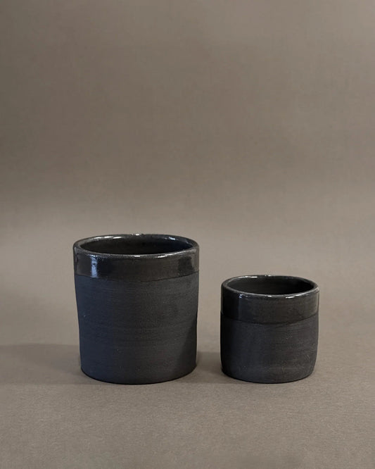 Two black ceramic cups, one larger and one smaller, with matte bodies and glossy rims on a gray background