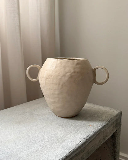 Handmade beige ceramic vase with two loop handles on rustic concrete table in minimal room