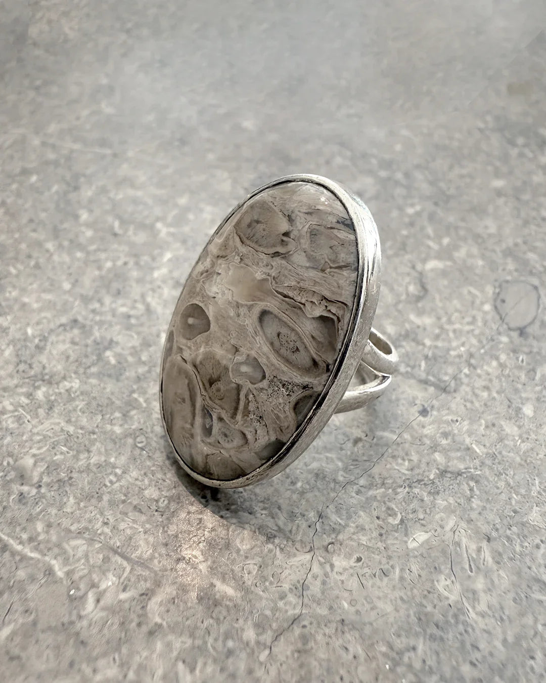 Silver ring with large oval gray fossil stone on textured gray surface