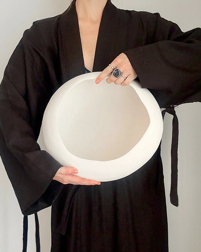 Person wearing black robe holding large white ceramic bowl against light background