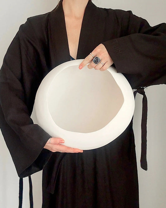 Person wearing black robe holding large white ceramic bowl against light background
