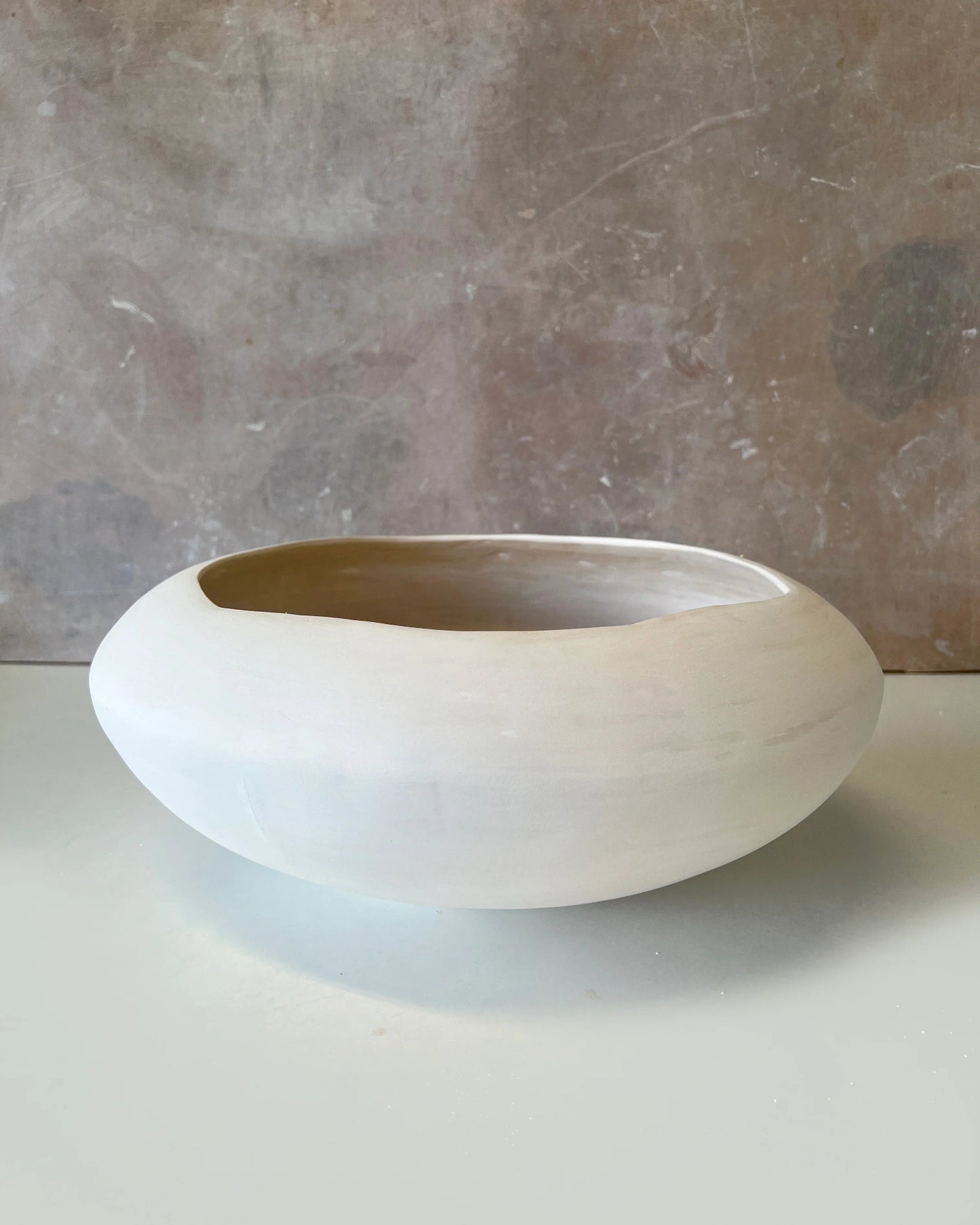 Minimalist round white ceramic bowl with a smooth matte finish on a light surface