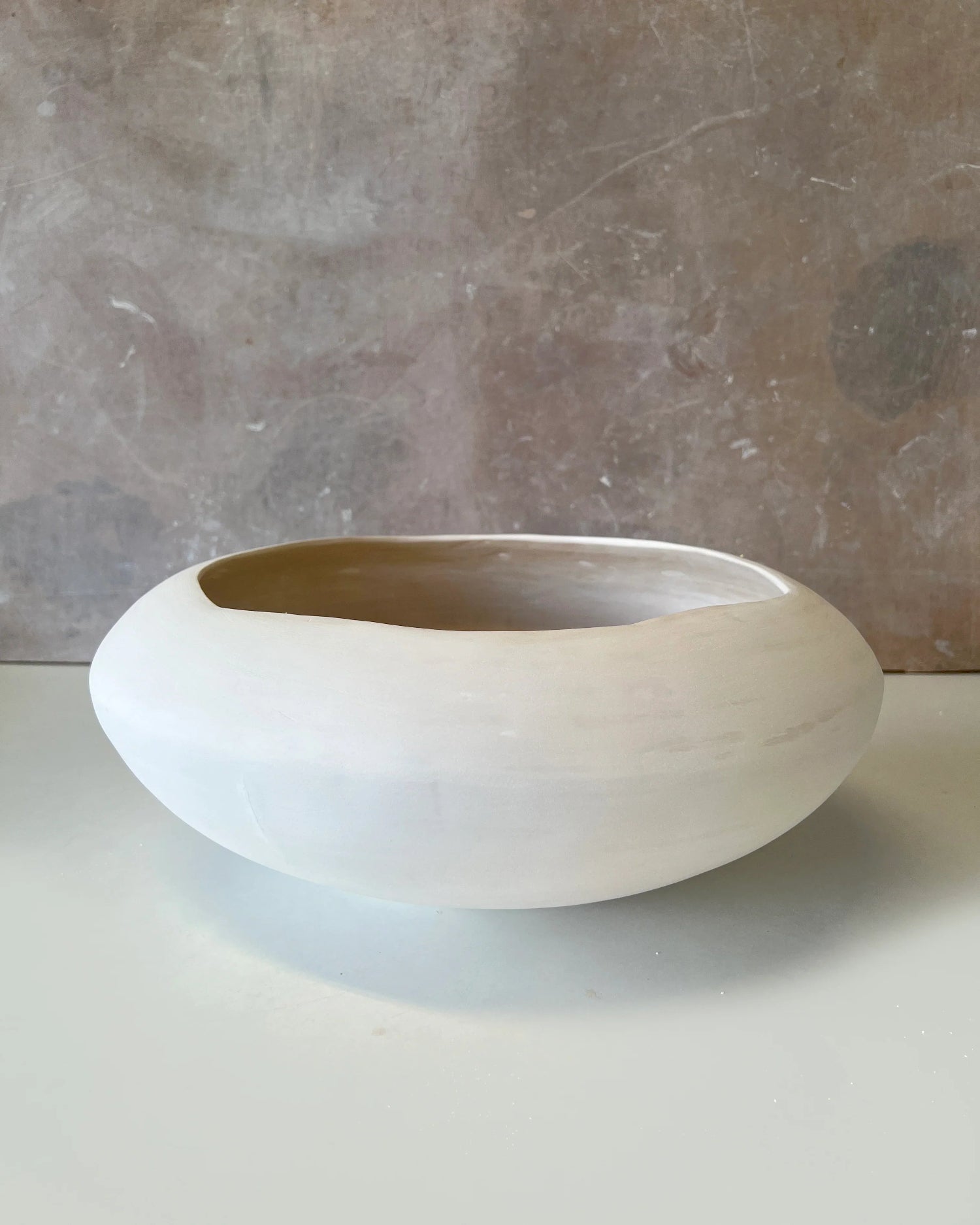 Minimalist round white ceramic bowl with a smooth matte finish on a light surface