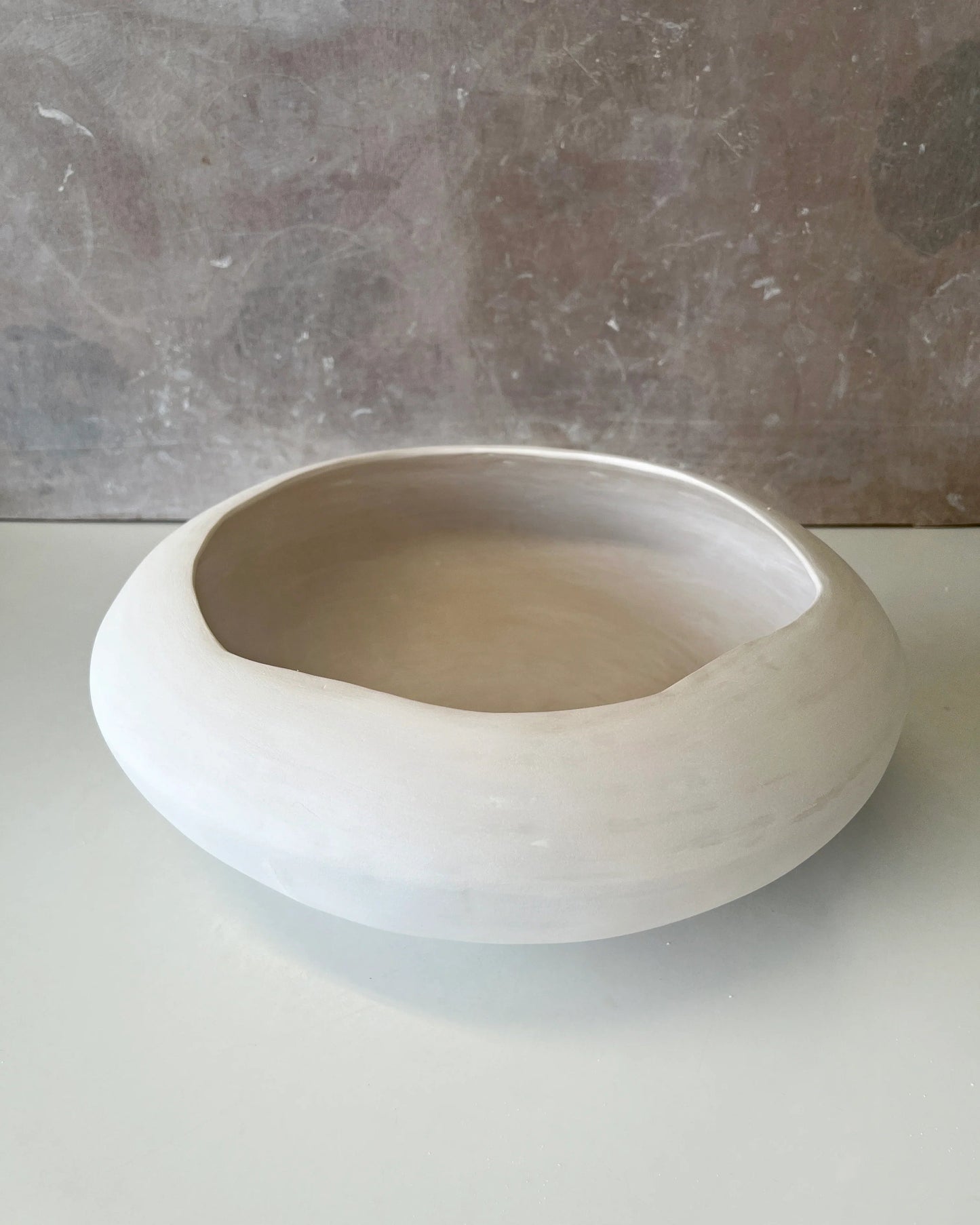 Minimalist round white ceramic bowl with smooth matte finish on a grey surface