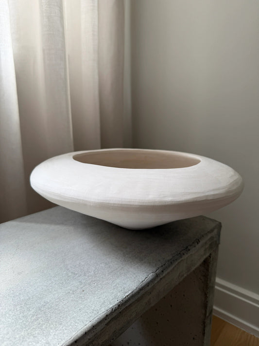 Minimalist white sculptural ceramic bowl on a concrete side table near light curtains