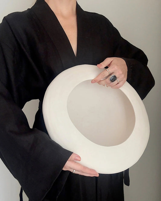 Person in black outfit holding large white wide-brimmed hat, styled with silver rings