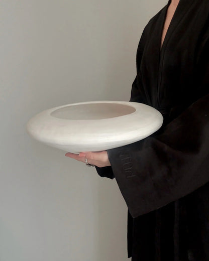 Person in black robe holding large white ceramic bowl with hollow center