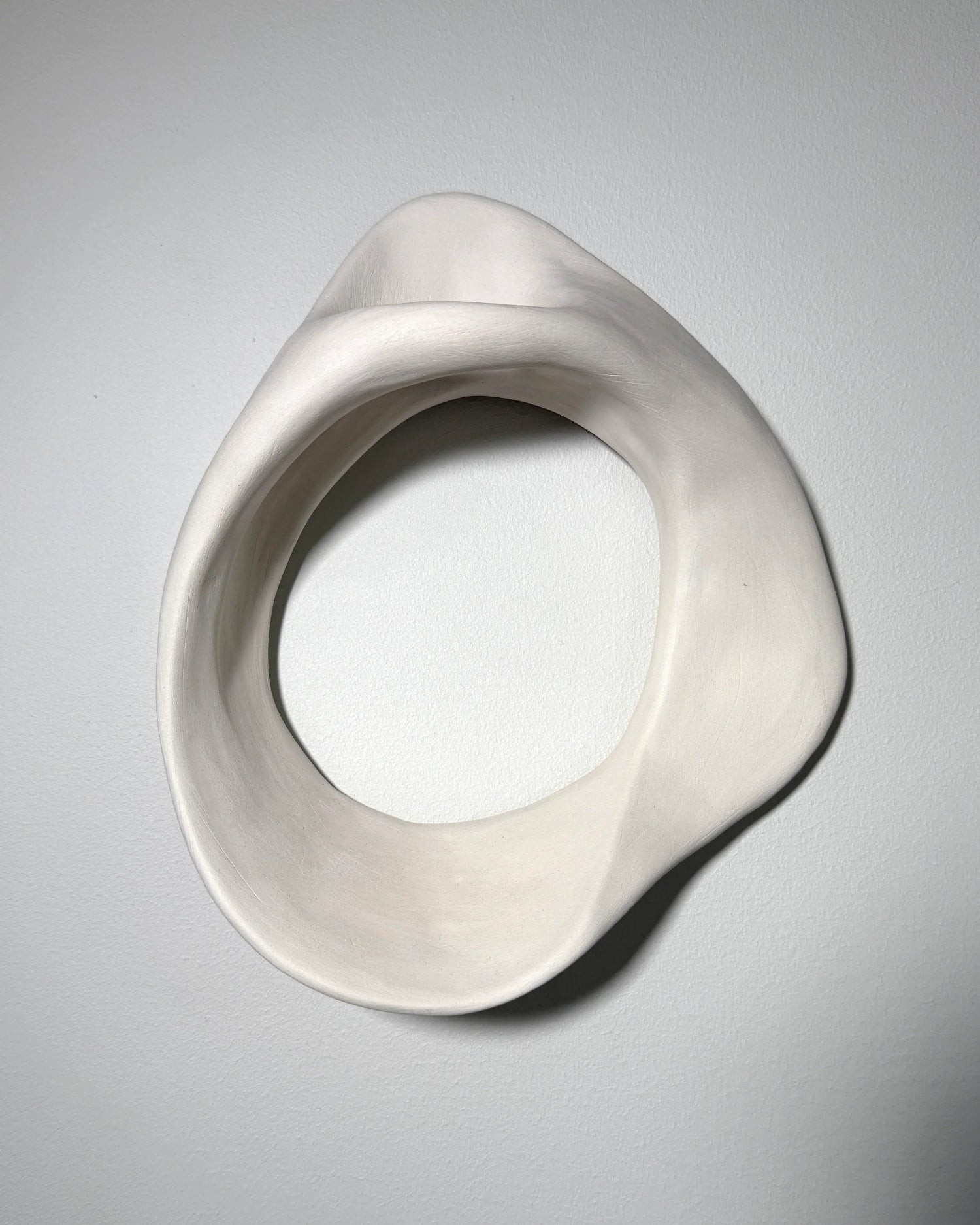 Smooth white ceramic abstract ring sculpture mounted on a plain white wall