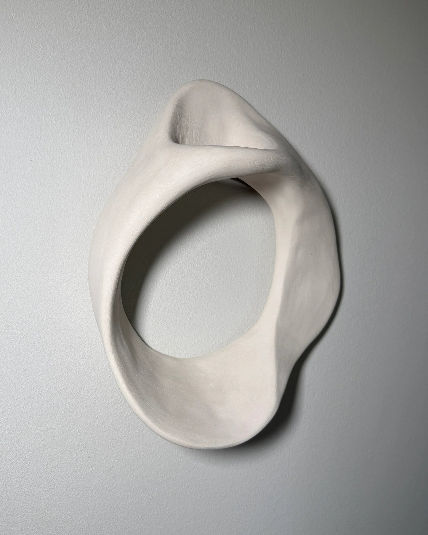 Abstract smooth white ceramic sculpture with flowing curves mounted on gray wall