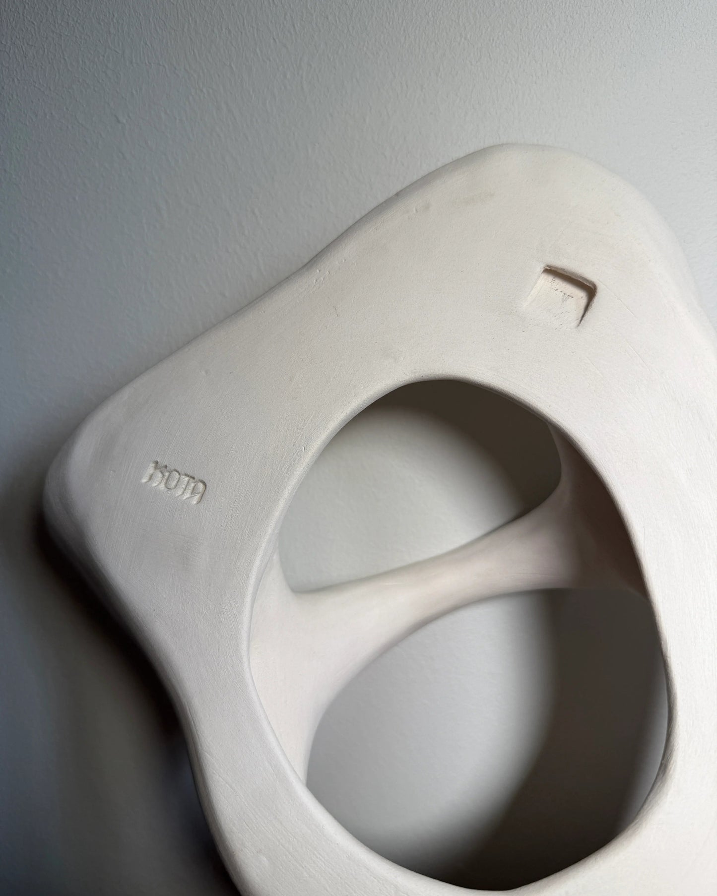 Abstract white ceramic hollow sculpture with smooth curves against gray wall