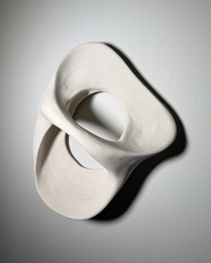 White abstract modern ceramic wall sculpture with smooth curved hollow shapes 