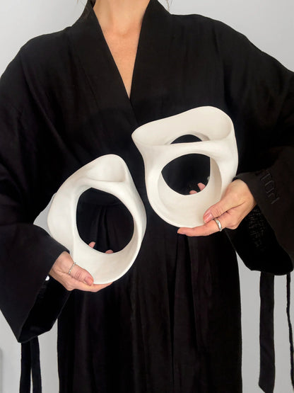Person in black robe holding two white abstract ceramic sculptures with holes