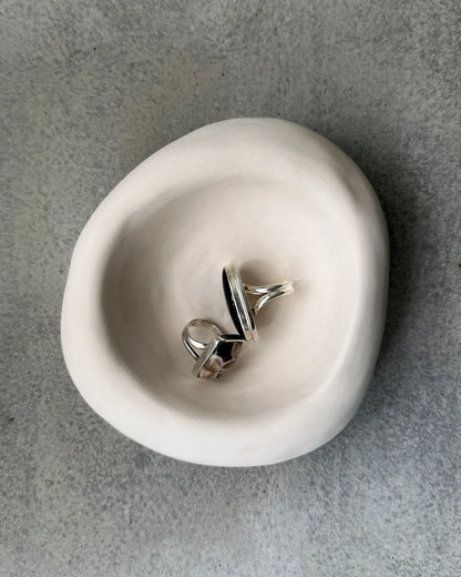 Two silver rings with black and patterned stones displayed in a smooth white ceramic bowl on gray stone surface