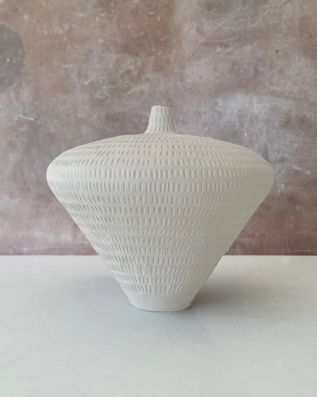 White textured ceramic vase with a rounded top and narrow base on a white surface