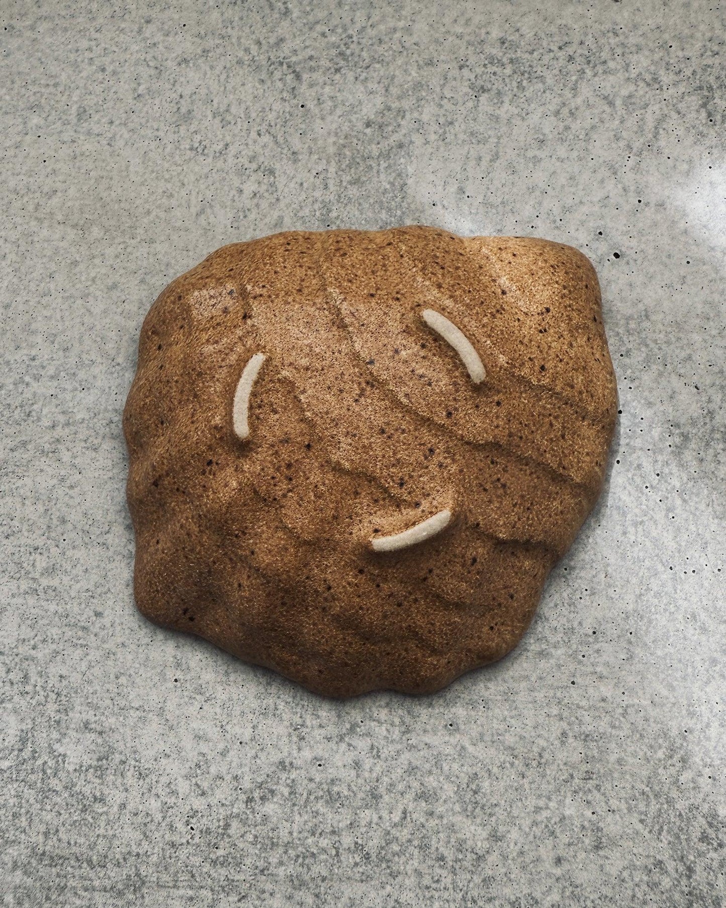 Brown speckled textured ceramic oyster plate with three white felt rests on concrete surface