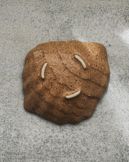 Brown speckled textured ceramic oyster plate with three white felt rests on concrete surface