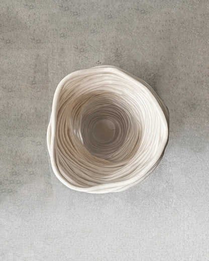 Top view of a white ceramic pot with wavy textured layers, placed on a gray surface