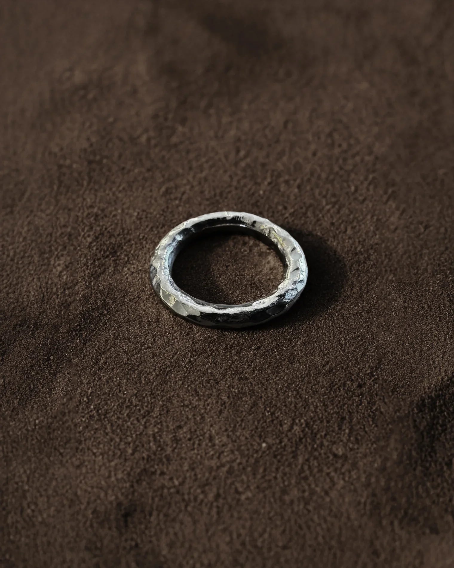Handcrafted hammered silver band ring on textured brown fabric background