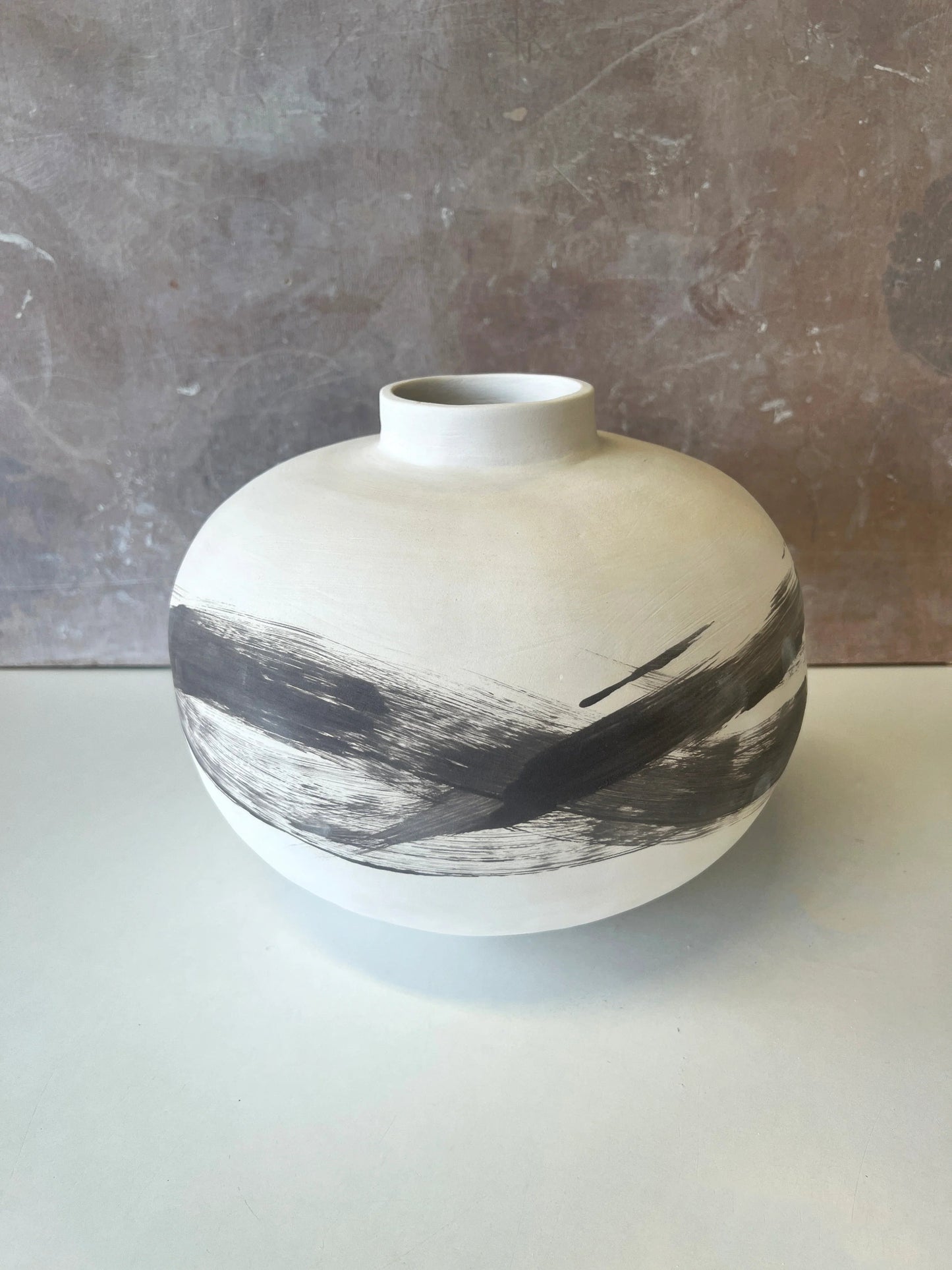White ceramic vase with round shape and wide black brushstroke design on a neutral surface
