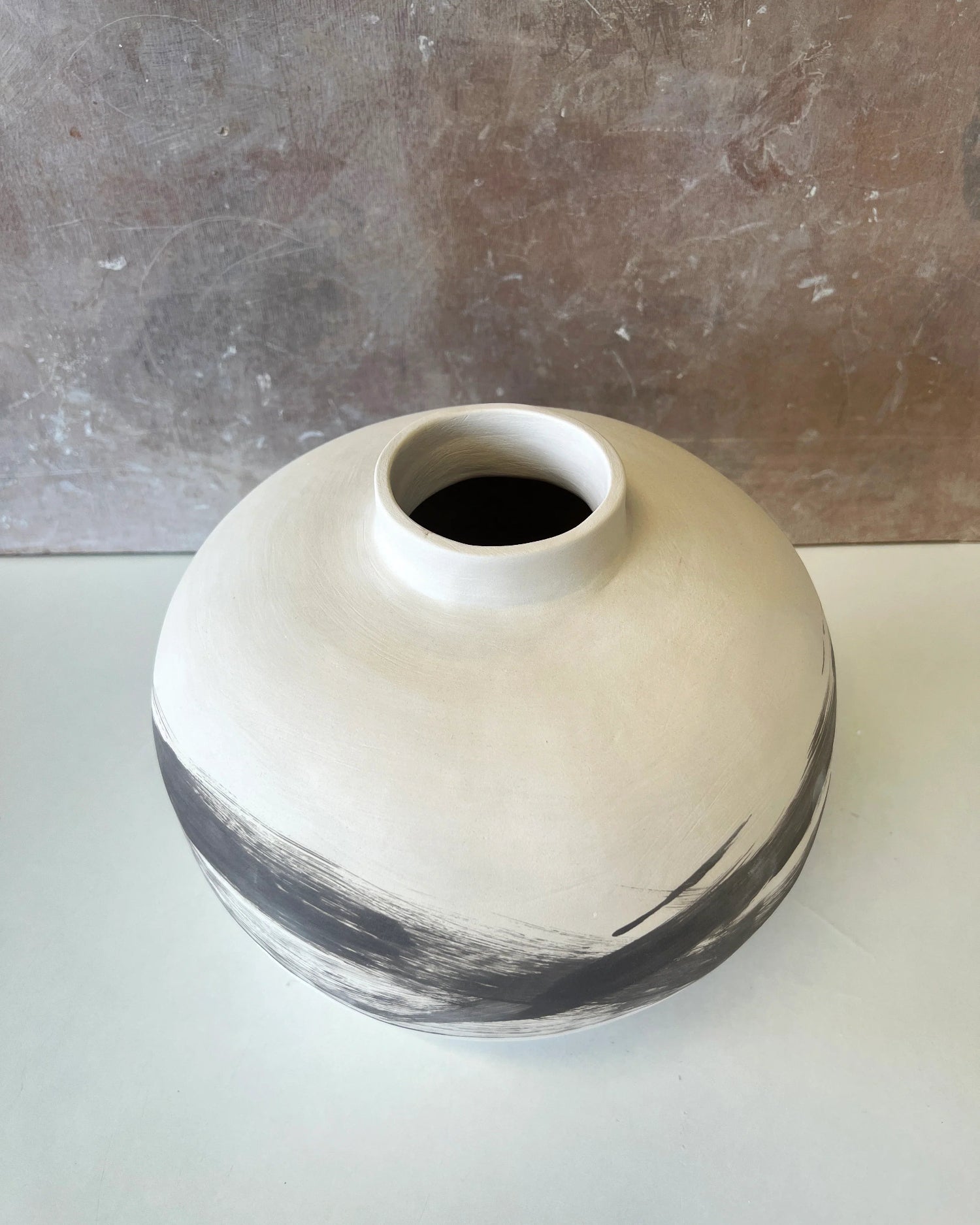 Round ceramic vase with wide mouth and black brushstroke design on white surface