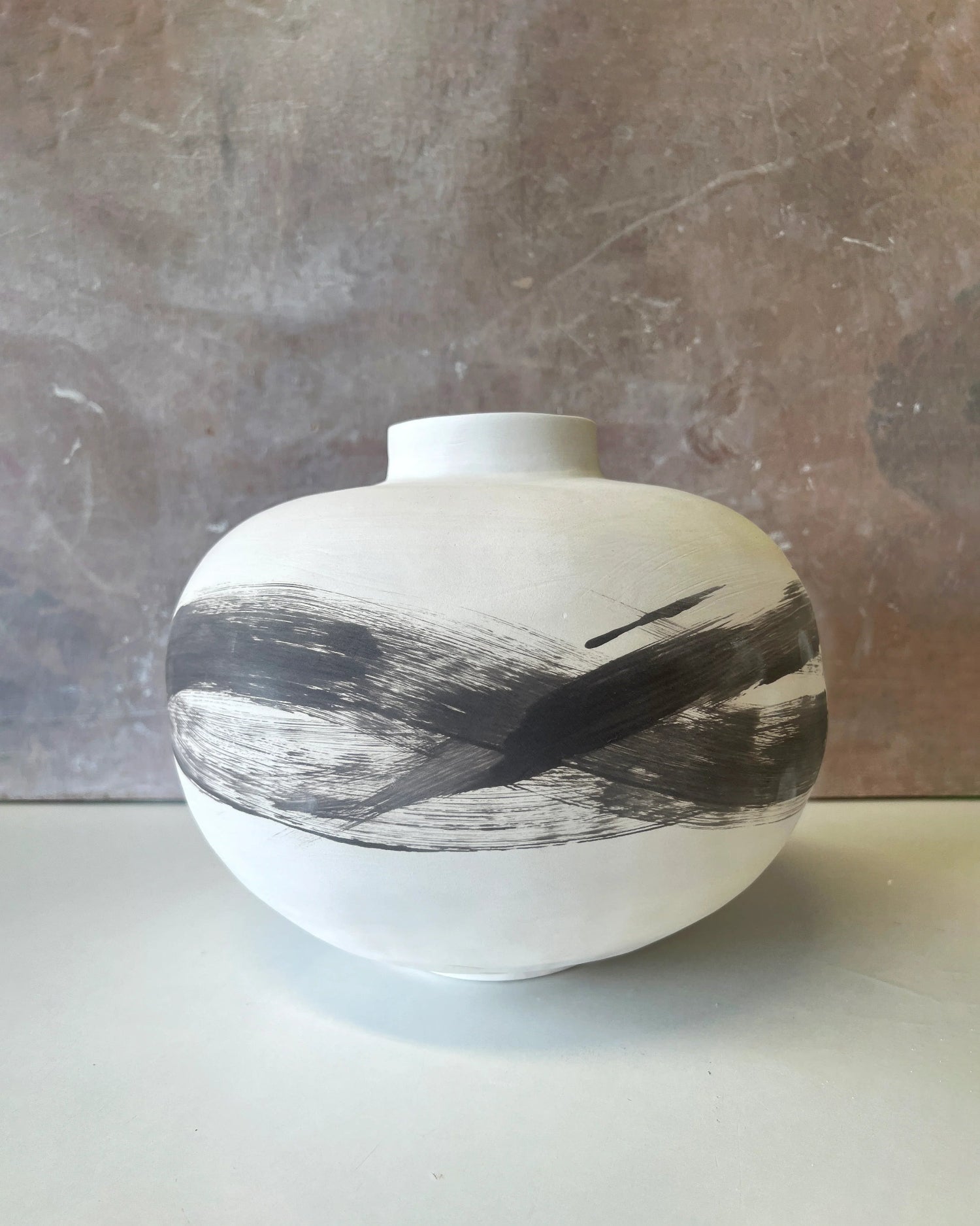White ceramic vase with wide round body and black abstract brushstroke design on neutral background