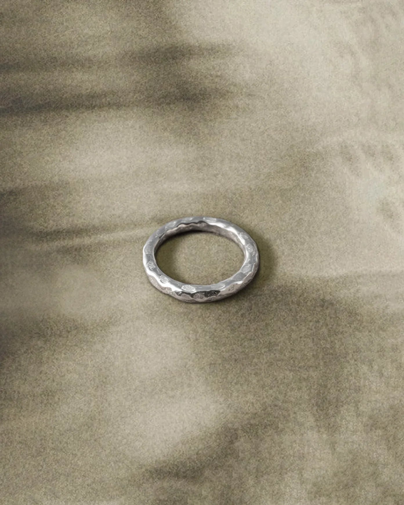 Handcrafted silver hammered band ring on textured beige fabric background